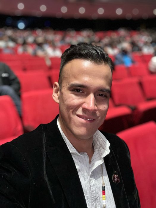 man in a black blazer smiles for photo while seated 