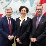 Three people stand in front of two Canadian flags.