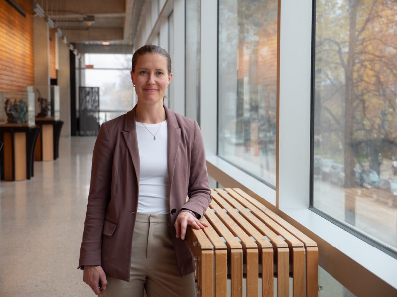 Dr. Kaarina Kowalec at a hallway, while standing and smiling at the camera.