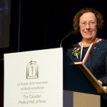 Dr. Estelle Simons stands at a lectern during her induction into the Canadian Medical Hall of Fame.