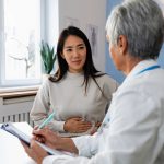 Patient describes stomach ache symptoms to doctor stock photo.
