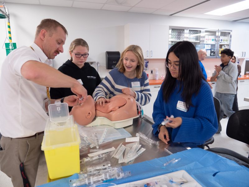 Instructor teaching three students how to perform a medical procedure on a manikin.