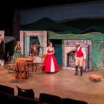 Six student actors performing on stage wearing period costumes from the 19th century.