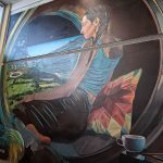 Echoes of the Earth mural by Mike Valcourt, an image of an Indigenous woman sitting in a Dyson ring with pillows and tea looking down at a futuristic version of Earth