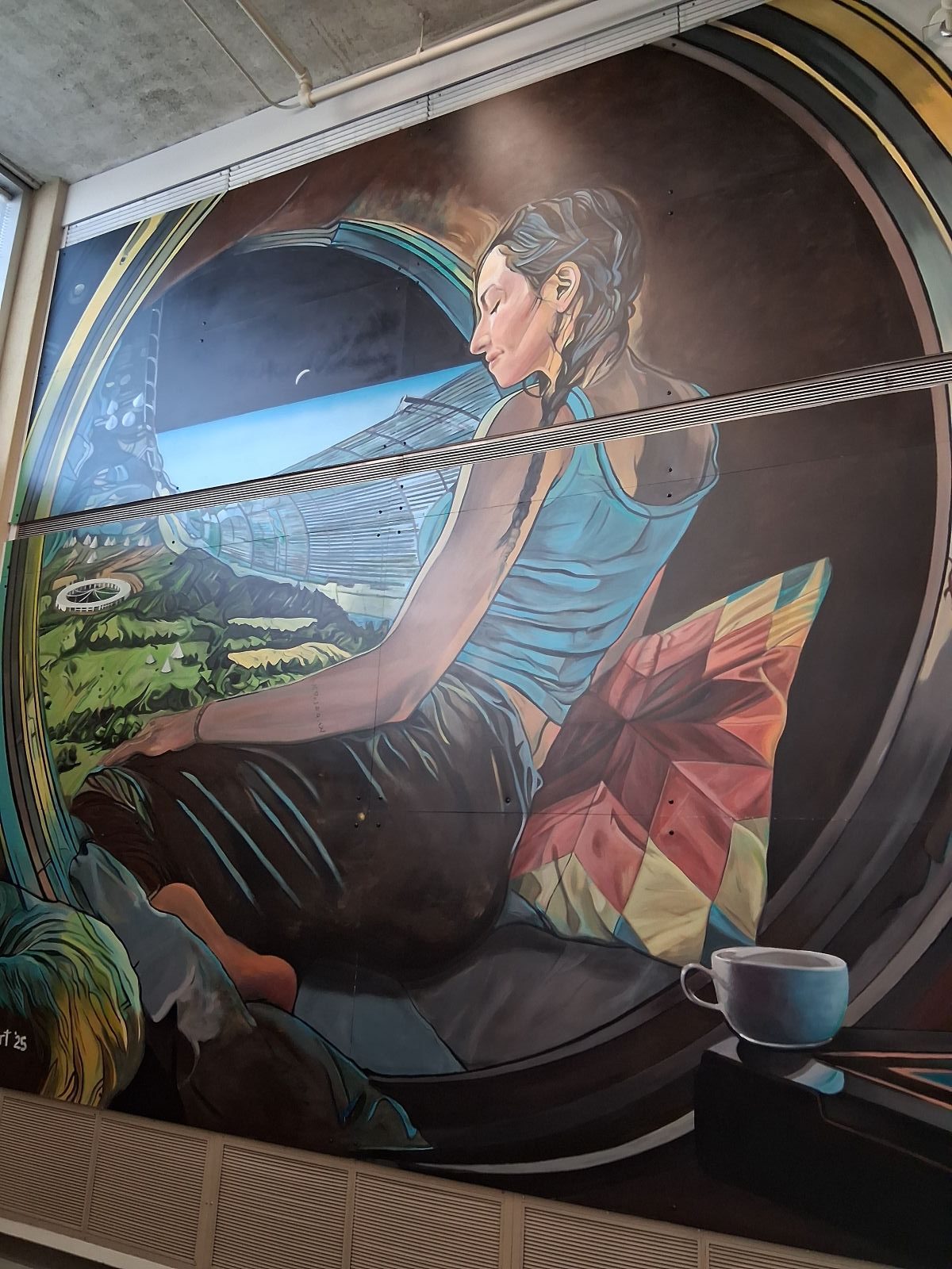 Echoes of the Earth mural by Mike Valcourt, an image of an Indigenous woman sitting in a Dyson ring with pillows and tea looking down at a futuristic version of Earth