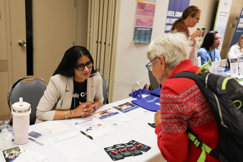 An attendee talks to a staff person at a booth, at the Age-Friendly University Showcase 2025.
