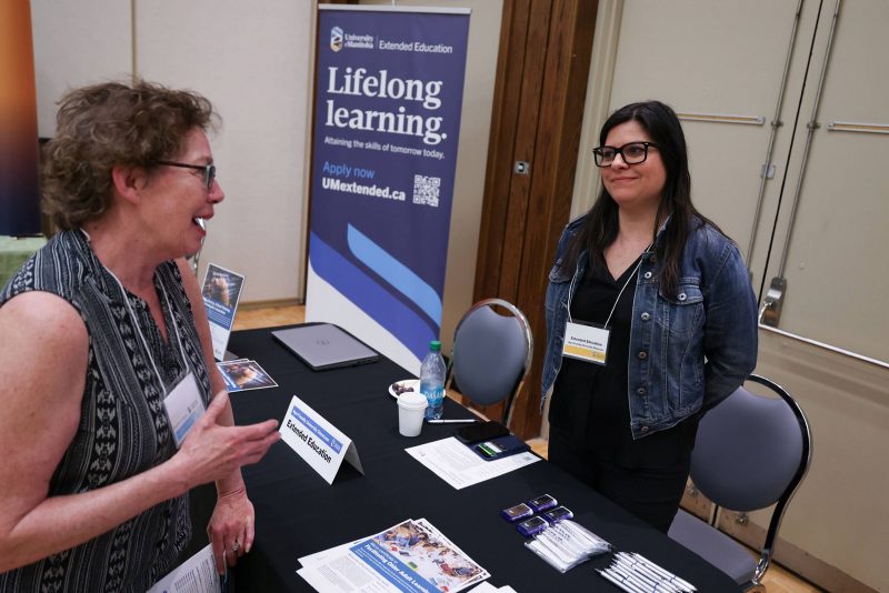 An attendee talks to a staff person at a booth, at the Age-Friendly University Showcase 2025.