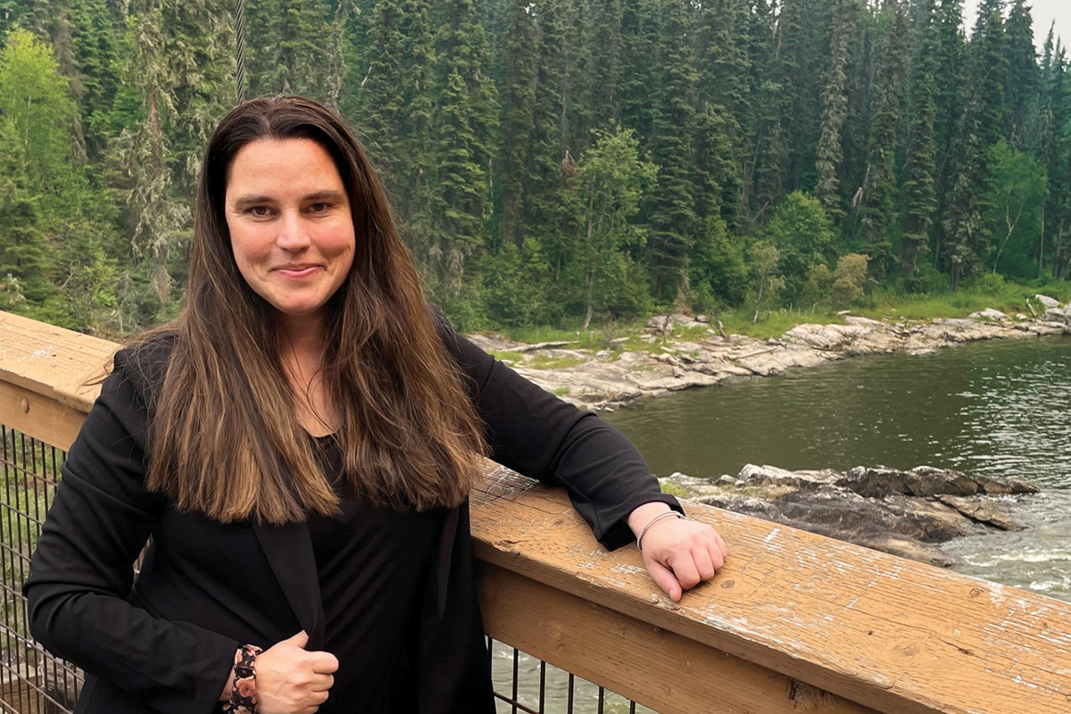 Cherie Murie stands near a river surrounded by trees.