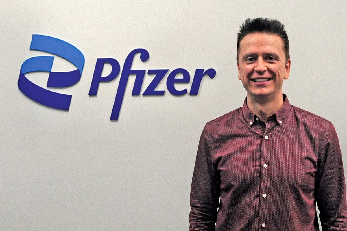 Daryl Fediuk standing and smiling at the camera, with the Pfizer logo in background.