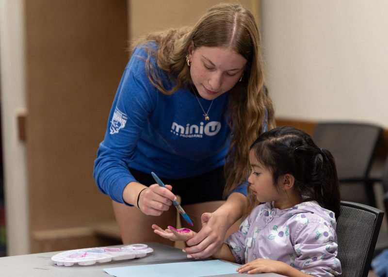 A Mini U leader working with a camper during an arts and crafts program