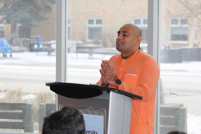 Sanatana Dharma Das, a monk from ISKCON of Manitoba, holds his hands together in prayer at a podium at Bannatyne campus.