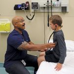 In an examination room, Dr. Jared Bullard lets a child hear his own heartbeat using a stethoscope.
