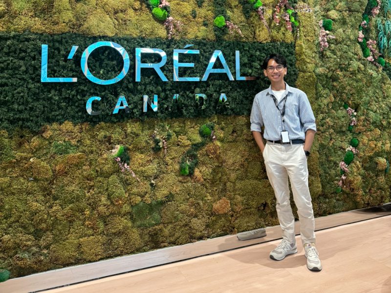 Jared Salvador smiling in front of a vertical garden wall featuring the L’Oréal Canada logo.