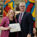 Two people smiling at the camera. Dr. Sheila Ng, on the left, is holding a certificate.