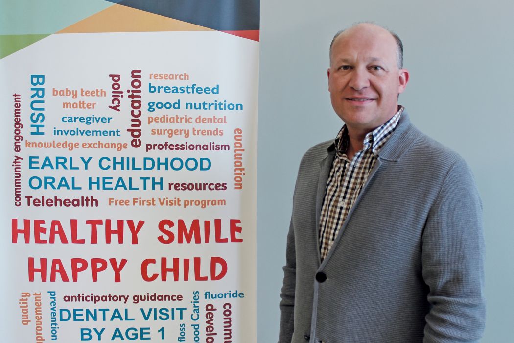 Dr. Bob Schroth next to a banner that reads "Healthy Smile Happy Child." There are also more than 20 terms and words related to oral health on the banner.