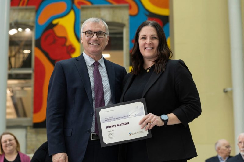 Two people smiling at the camera. Kristi Watson, on the right, is holding a certificate.