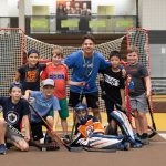 A Mini U leader posing with a group of campers during a floor hockey session