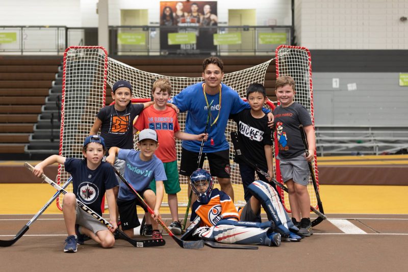 A Mini U leader posing with a group of campers during a floor hockey session.