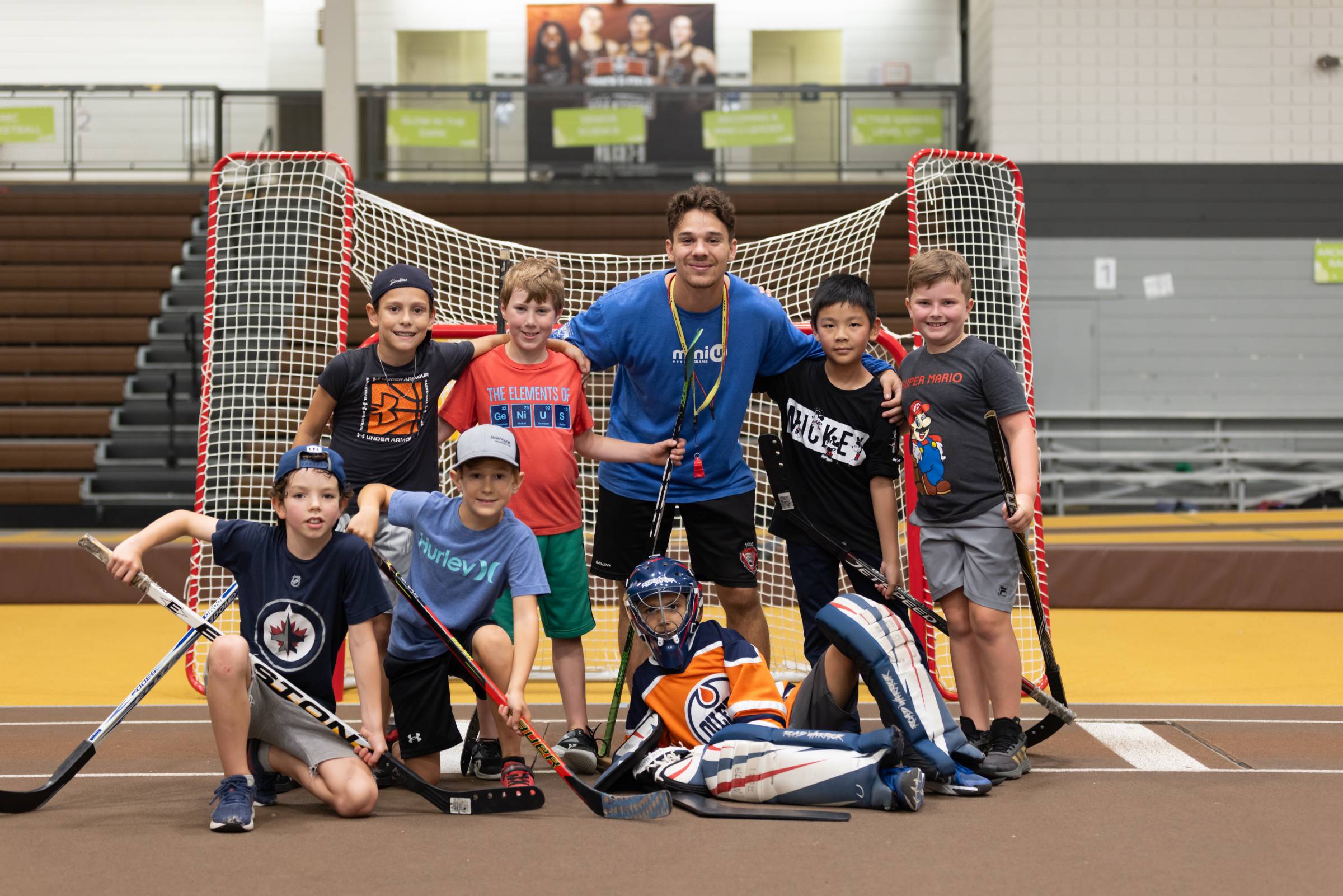 A Mini U leader posing with a group of campers during a floor hockey session