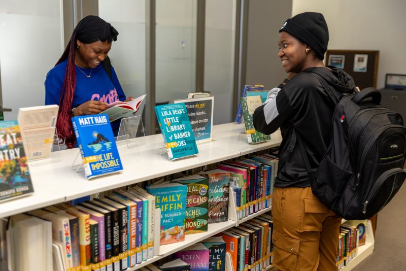 Two students browsing a bookshelf of colourful books