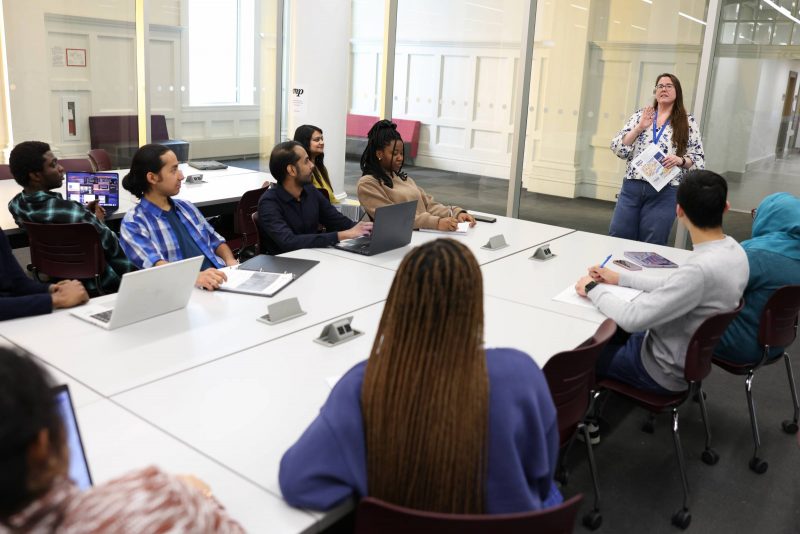 A library staff member teaching a group of students sitting at a table