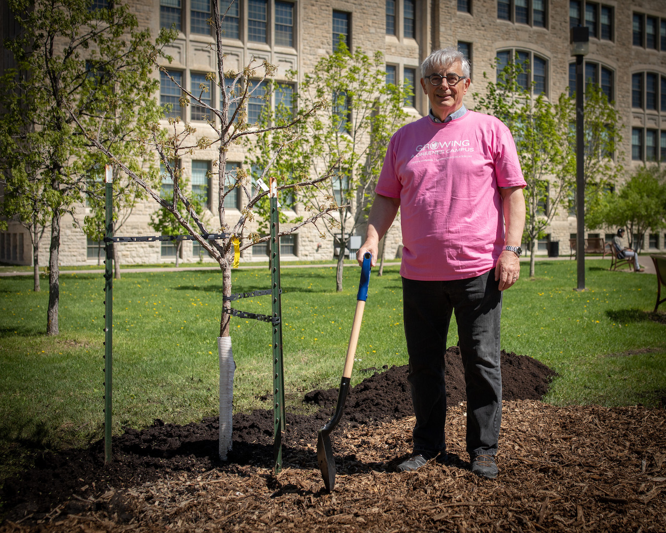 President Emeritus David Barnard stands beside his just-planted tree, shovel in hand.