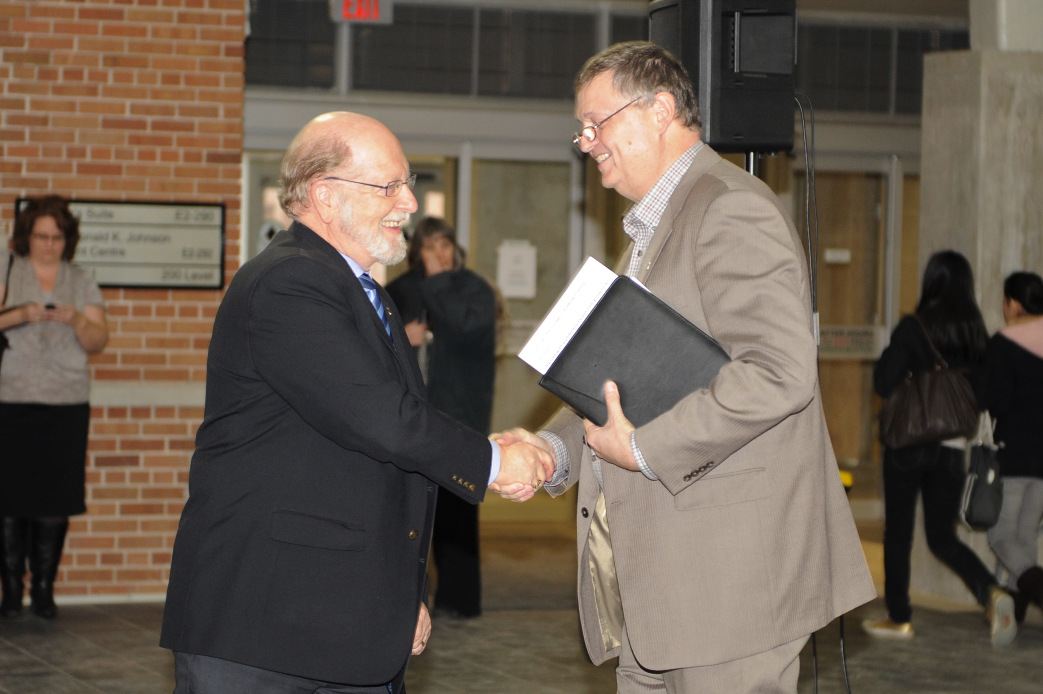 Alt: Doug Ruth shakes hands with Ron Britton in candid photo.