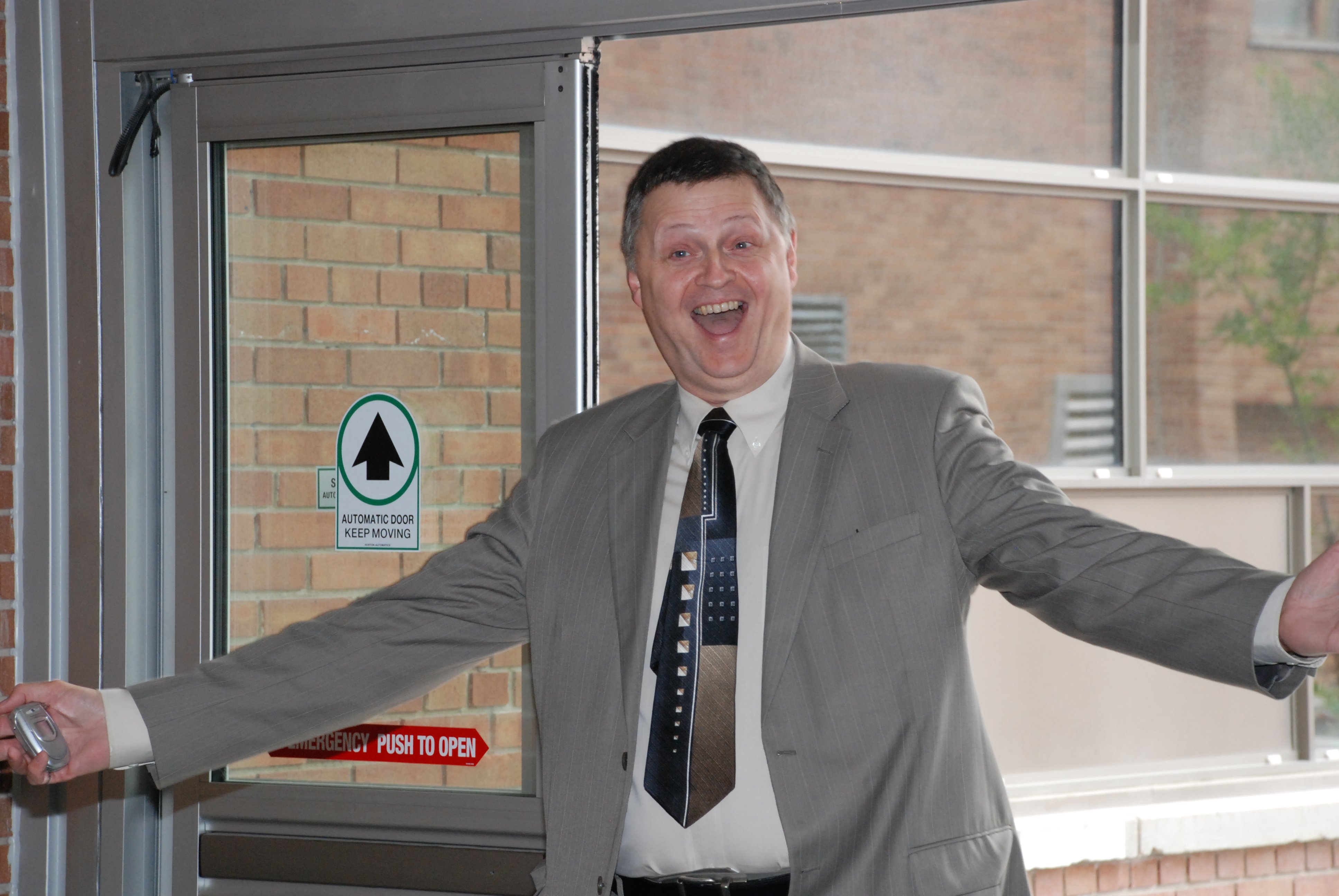 Alt: Doug Ruth entering building with a large, open mouth smile and arms extended with enthusiasm.